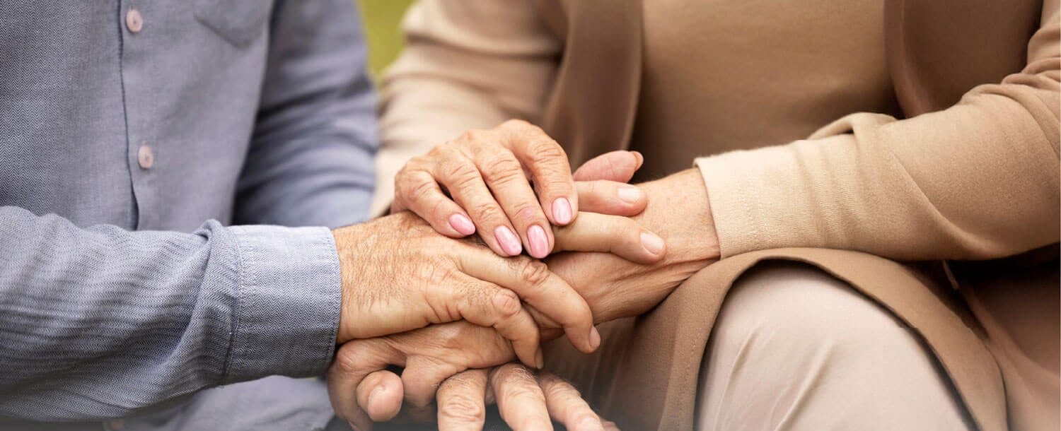 An older couple holding hands, seated together